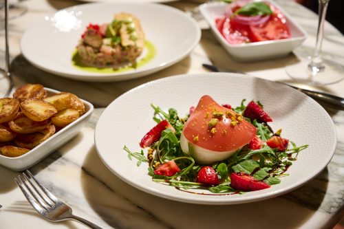 Caprese-inspired salad with sliced tomato, mozzarella, arugula, strawberries, and pistachio crumble.