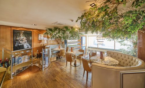 Upscale restaurant interior with hanging greenery, wooden floors, and tufted booths.