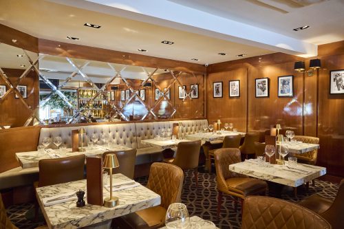 Elegant restaurant dining area with marble-topped tables, tufted brown leather chairs, and a diamond mirror wall configuration.