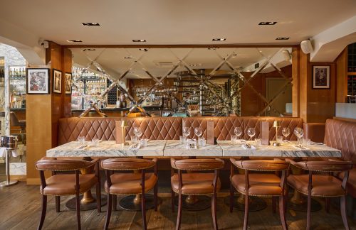 Upscale dining area with a long marble table, tufted leather seating, and a diamond-mirror wall in a bar/restaurant setting.