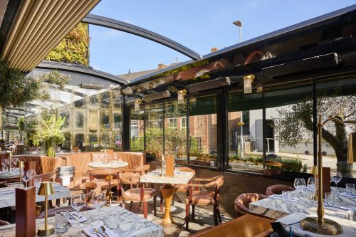 Sunlit restaurant dining area with pink leather booths, marble tables, and glass walls.