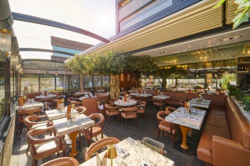 Open-air restaurant dining area with marble-topped tables, brown leather chairs, and a central tree pillar in the courtyard.