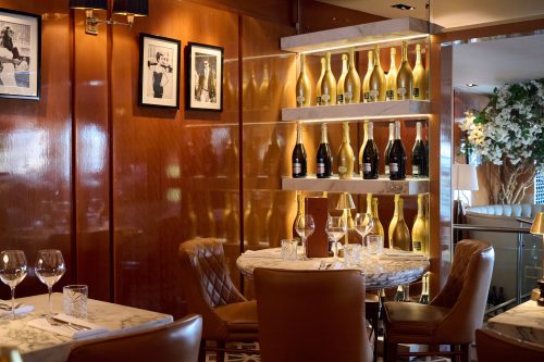 Upscale dining area with a wine display on marble shelves against a polished wood wall and framed black-and-white photos.