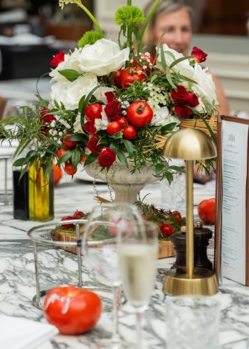 Elegant bouquet centerpiece with white and red roses, green foliage, and small tomatoes on a marble table surface