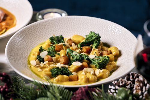 Creamy pasta with broccoli rabe, croutons and almond slices in a textured white bowl.