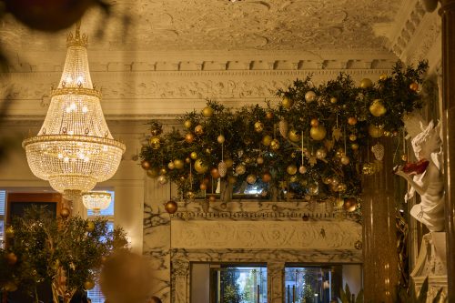 Grand chandelier and festive greenery with gold ornaments in an ornate marble room interior